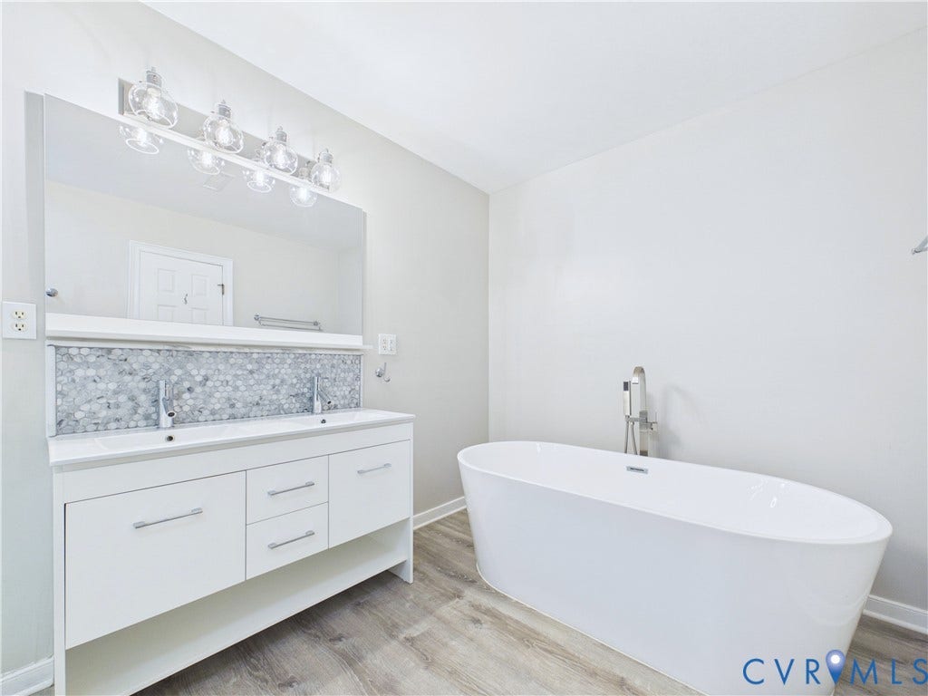 4515 Exton Lane, Chester, VA 23831 Freestanding soaking tub, double vanity with dual sinks, hexagonal tile backsplash, wood-finish flooring, and a large wall-mounted mirror