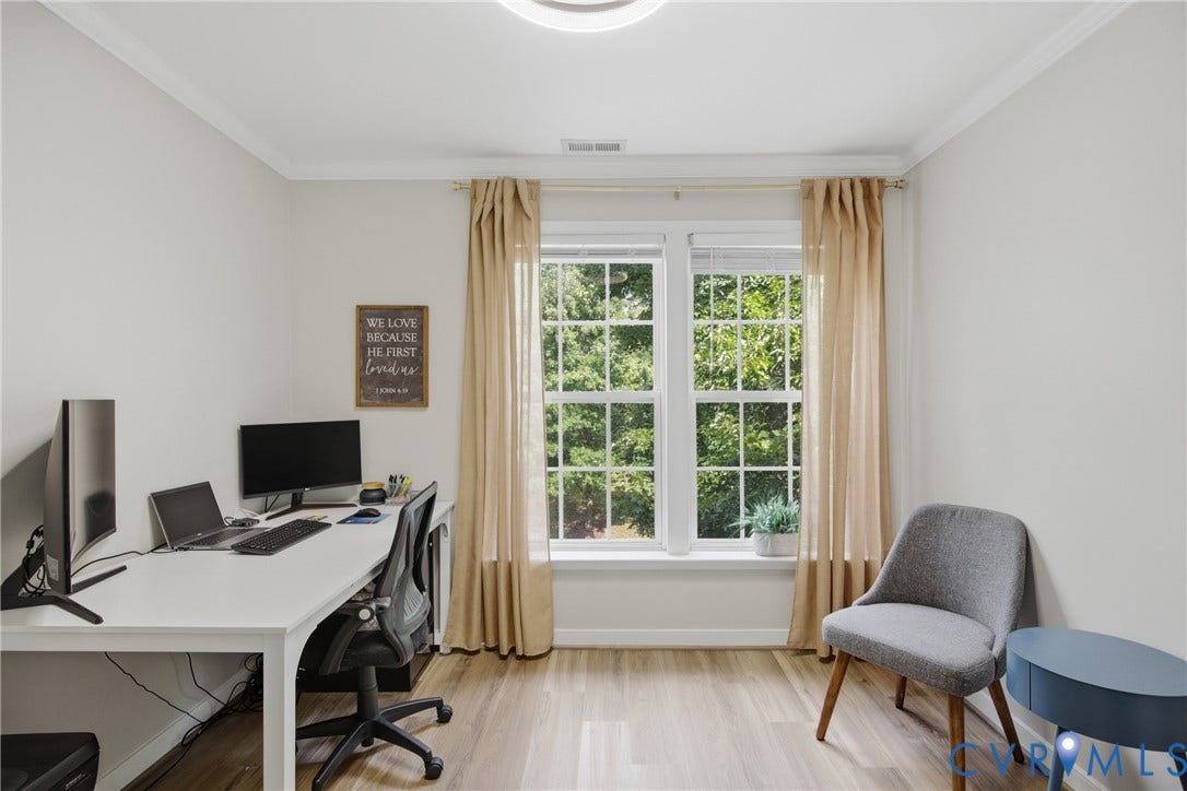 Bright room featuring wood-finish flooring, white walls, and a large window with muntins overlooking mature trees