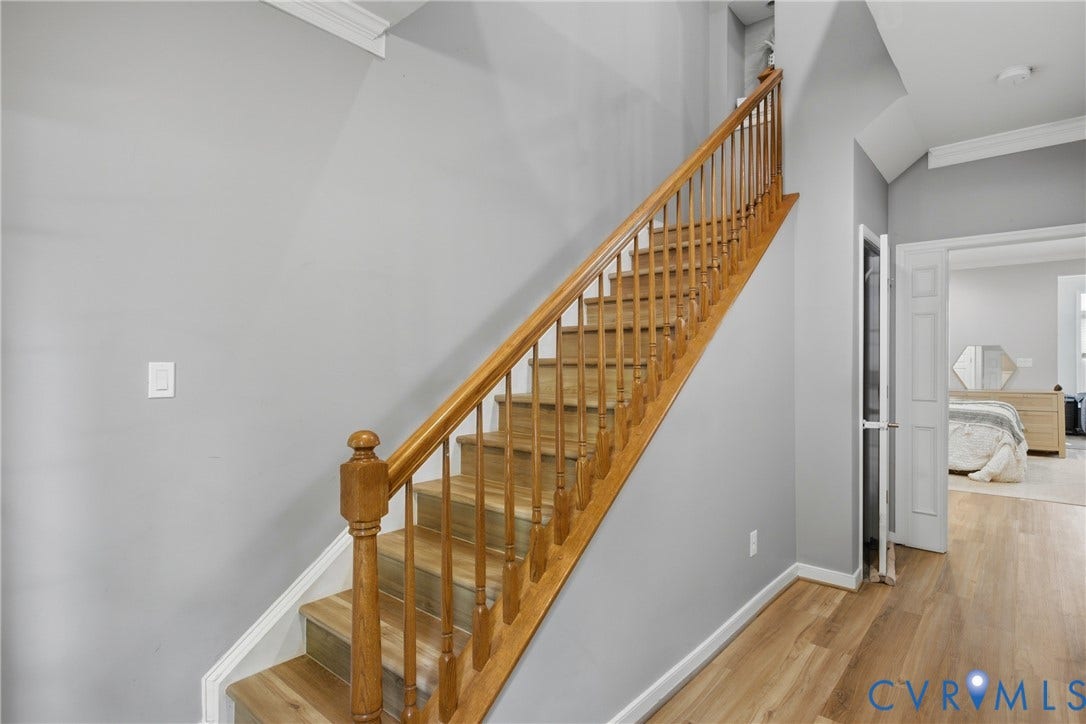 Light wood-finish staircase with wood balusters and railing, complemented by neutral wall paint and white trim