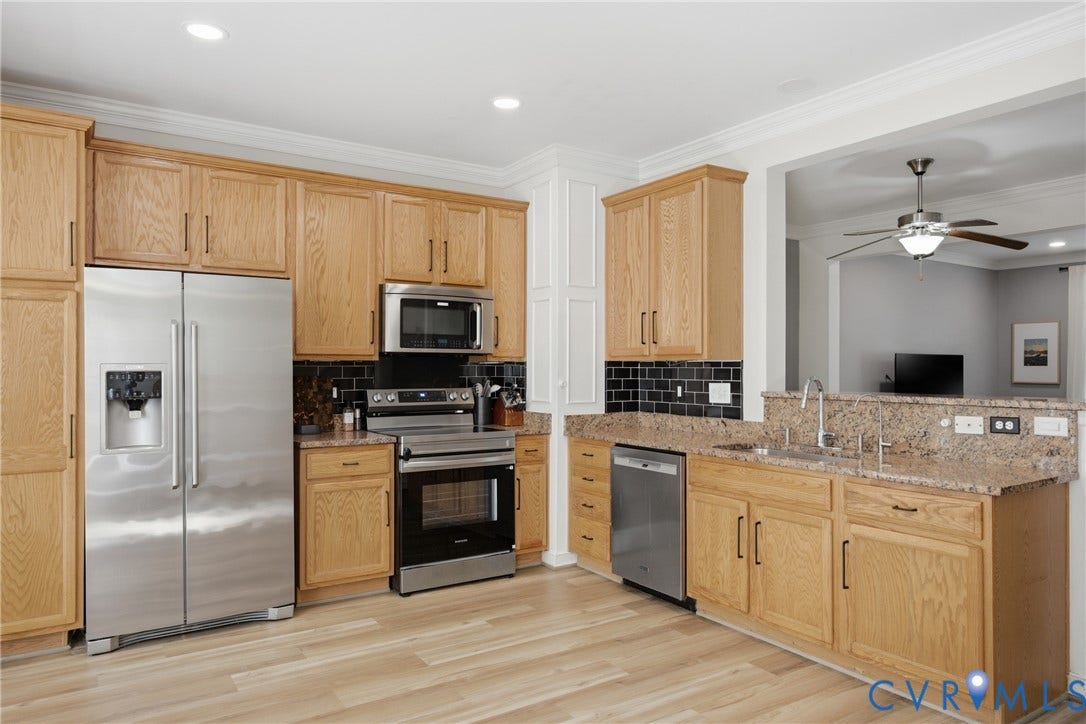Kitchen featuring light wood-finish cabinetry, stainless steel appliances, a black subway tile backsplash, and granite countertops