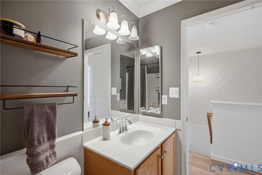 Spa-inspired bathroom featuring a framed mirror with integrated vanity lighting, white quartz countertop, warm wood-finish cabinetry, polished chrome fixtures, and ceramic undermount sink