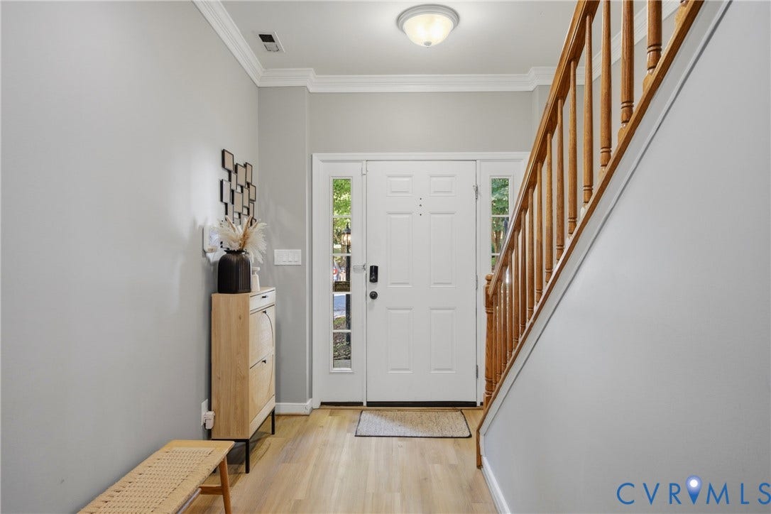 Entryway featuring a white paneled door with sidelights, wood-finish flooring, and a natural wood staircase with balusters