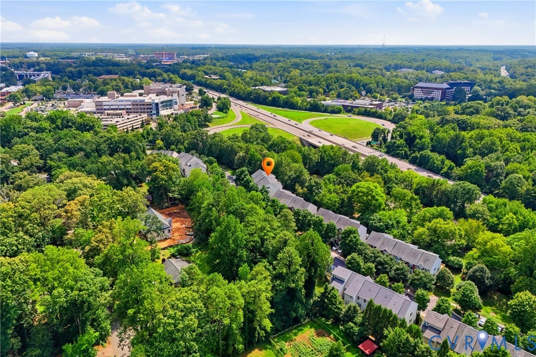 Aerial perspective showcasing a community of townhomes nestled amongst mature trees, with a prominent highway system and institutional buildings in the background