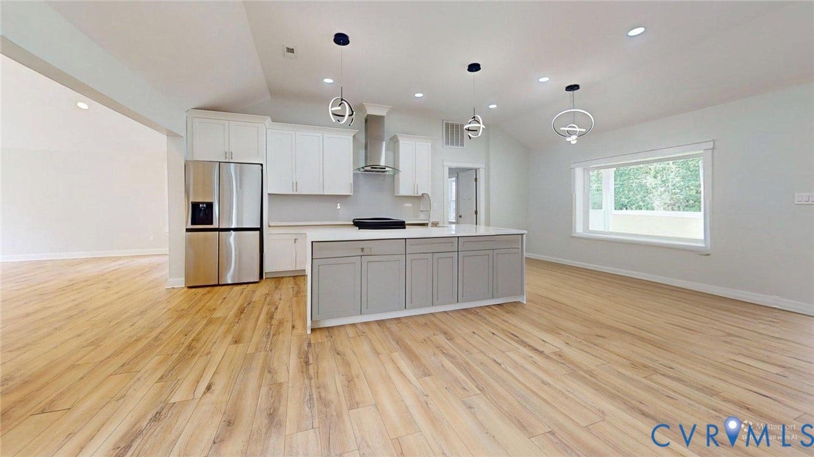 Modern kitchen featuring a central island with a light countertop, white upper cabinetry, grey lower cabinetry, stainless steel appliances, and wood-finish flooring