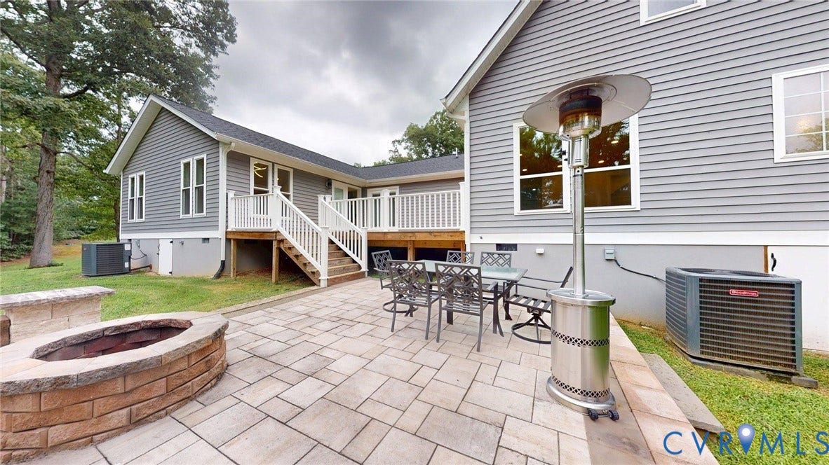 Spacious paver patio featuring a built-in stone fire pit, a multi-level deck with white railings, and gray siding exterior