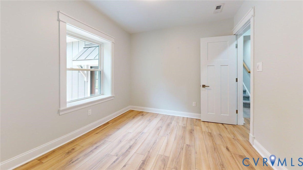 Light-filled interior space featuring wood-finish flooring, crisp white baseboards, and a large single-hung window with decorative trim