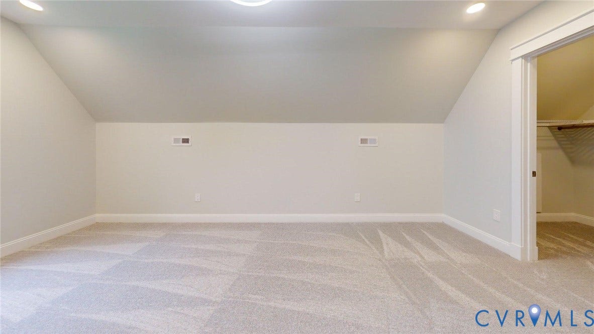 Spacious room featuring vaulted ceilings, light-toned carpeting, recessed lighting, and a closet with built-in shelving