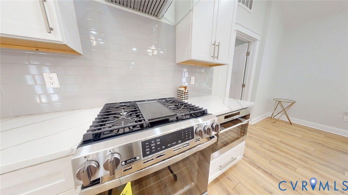 Stainless steel gas range with a griddle, white subway tile backsplash, white shaker-style cabinetry, white countertops, and wood-finish flooring