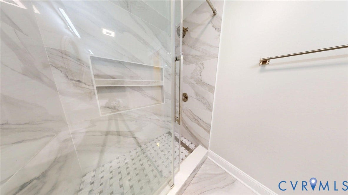 Walk-in shower featuring glass enclosure and full-height marbled tile surround