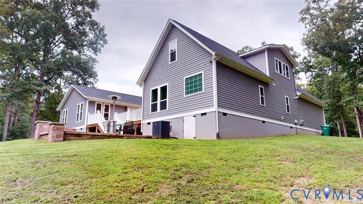 Gray horizontal siding exterior with white trim, multiple windows, a sloped terrain, and a visible air conditioning unit