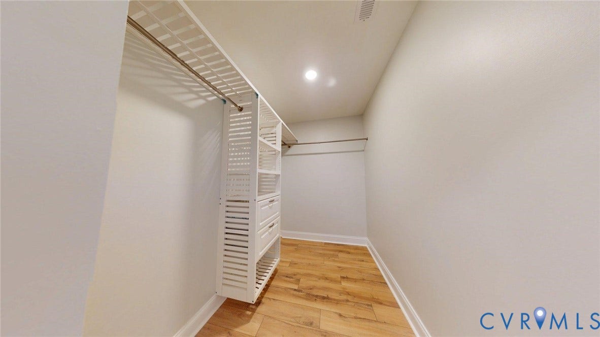 Walk-in closet featuring light wood-finish flooring, white walls, recessed ceiling lighting, and a built-in shelving system with drawers
