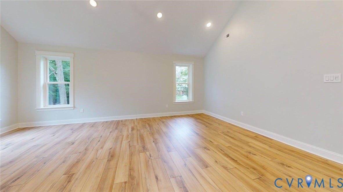 Bright and spacious room showcasing gleaming wood-finish flooring, recessed lighting throughout the ceiling, and abundant natural light from two large windows