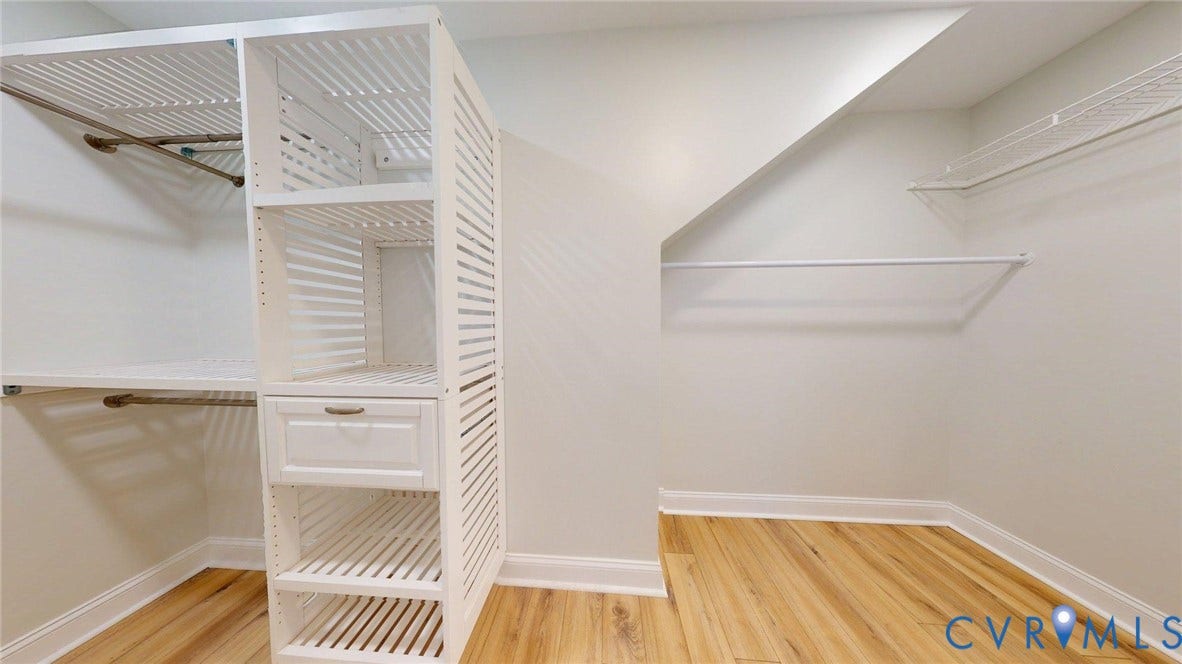Well-appointed closet featuring custom white shelving, integrated drawer storage, multiple hanging rods, and wood-finish flooring