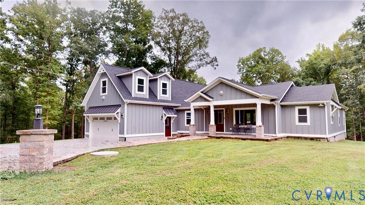 Contemporary-style exterior featuring gray siding, a covered front porch with stone accents, a two-car garage, and a gravel driveway with a stone pillar