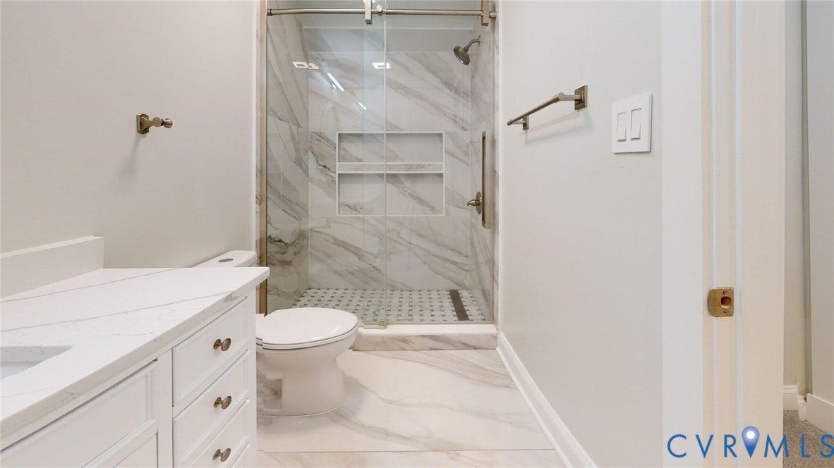 Spa-inspired primary bathroom featuring a walk-in shower with marble-look tile surround and built-in shelving, dual vanity with white cabinetry and brushed nickel hardware, porcelain tile flooring, and contemporary chrome fixtures throughout