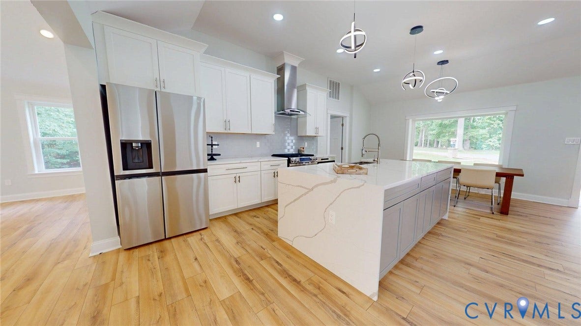 Modern kitchen featuring a large waterfall island with quartz countertop, stainless steel appliances, recessed lighting, and wood-finish flooring