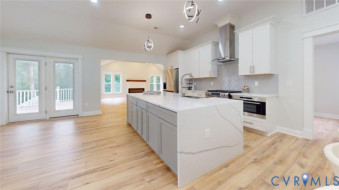 Kitchen featuring a waterfall island with quartz countertop, light wood-finish flooring, white cabinetry, stainless steel appliances, and double glass-paneled doors leading to an exterior deck