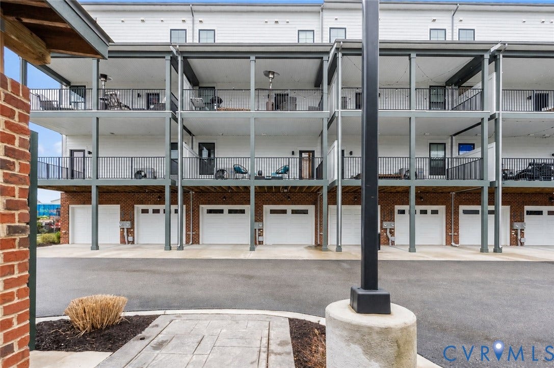 2439 Ownby Lane, #B 13, Richmond, VA 23220 Modern multi-unit residential building featuring three levels of apartments with private balconies, ground-floor garage parking with overhead doors, steel support columns, and brick exterior detailing