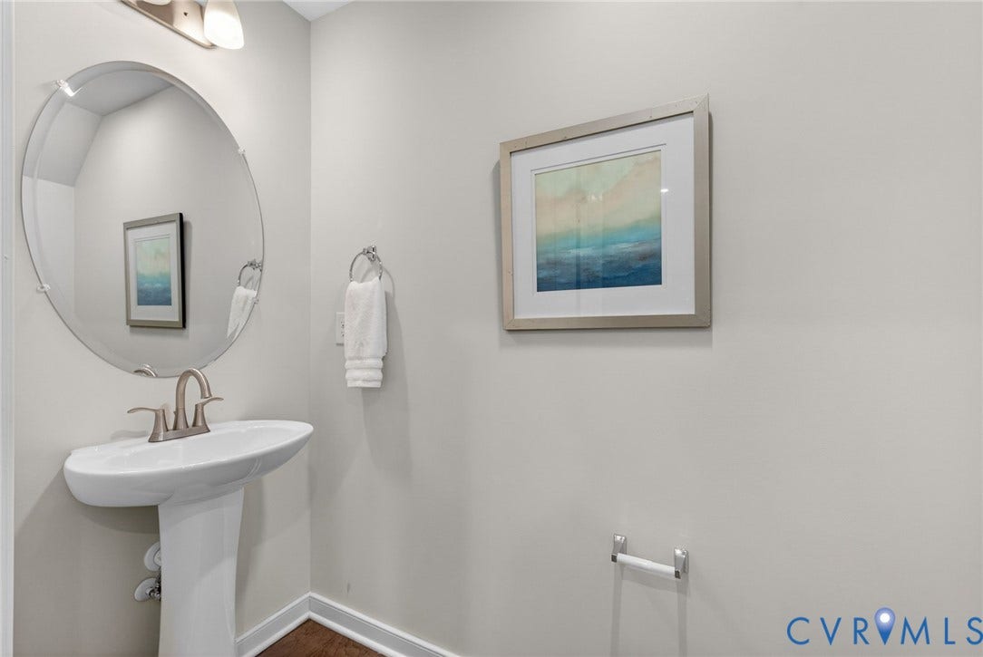 2439 Ownby Lane, #B 13, Richmond, VA 23220 Pedestal sink with brushed nickel faucet, large oval mirror, and wall-mounted vanity lighting