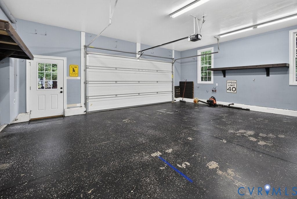 8825 First Branch Lane, Chesterfield, VA 23838 Spacious garage featuring a sectional overhead door, a pedestrian door with windowpanes, multiple windows, built-in shelving, and overhead lighting