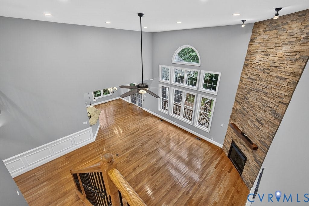 8825 First Branch Lane, Chesterfield, VA 23838 Two-story living area featuring wood-finish flooring, a stone-clad fireplace with a wood mantle, a multi-pane window array, and a ceiling fan
