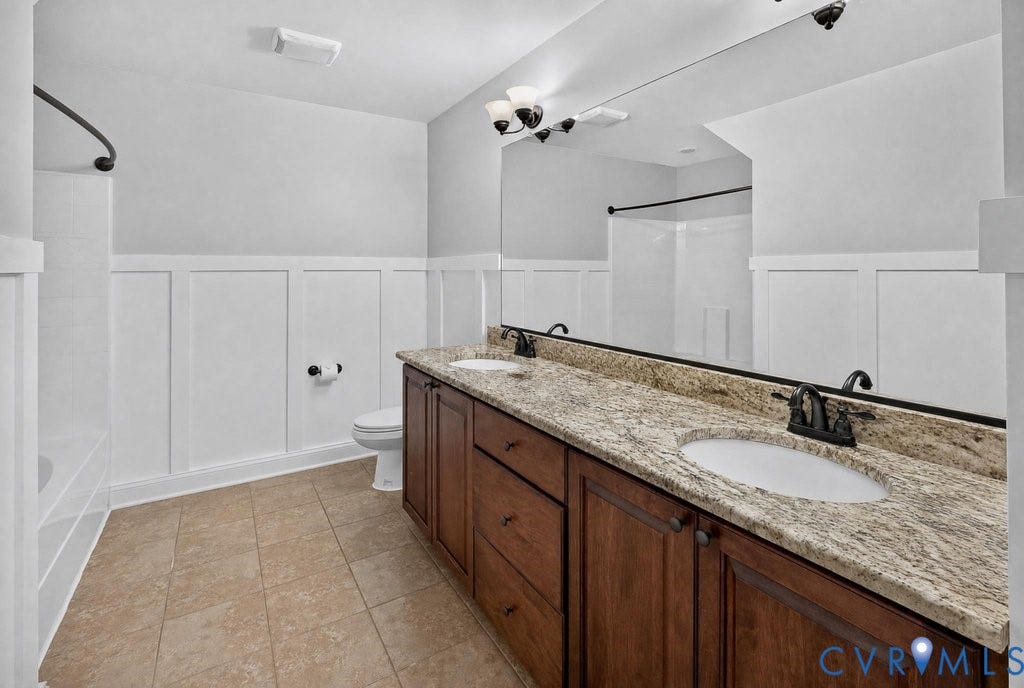8825 First Branch Lane, Chesterfield, VA 23838 Double vanity with integrated sinks, granite countertop, rich wood-finish cabinetry, wainscoting, and large wall-mounted mirror