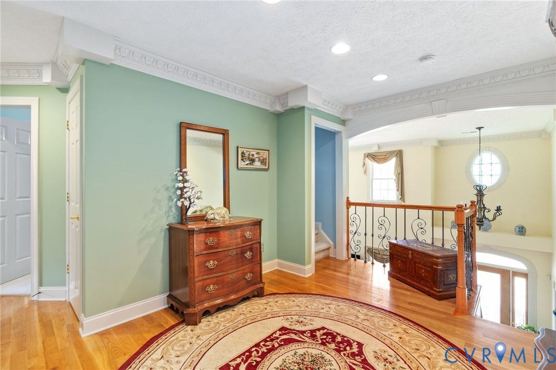 Upper-level landing featuring hardwood flooring, detailed crown molding, arched entryways, and wrought iron balusters