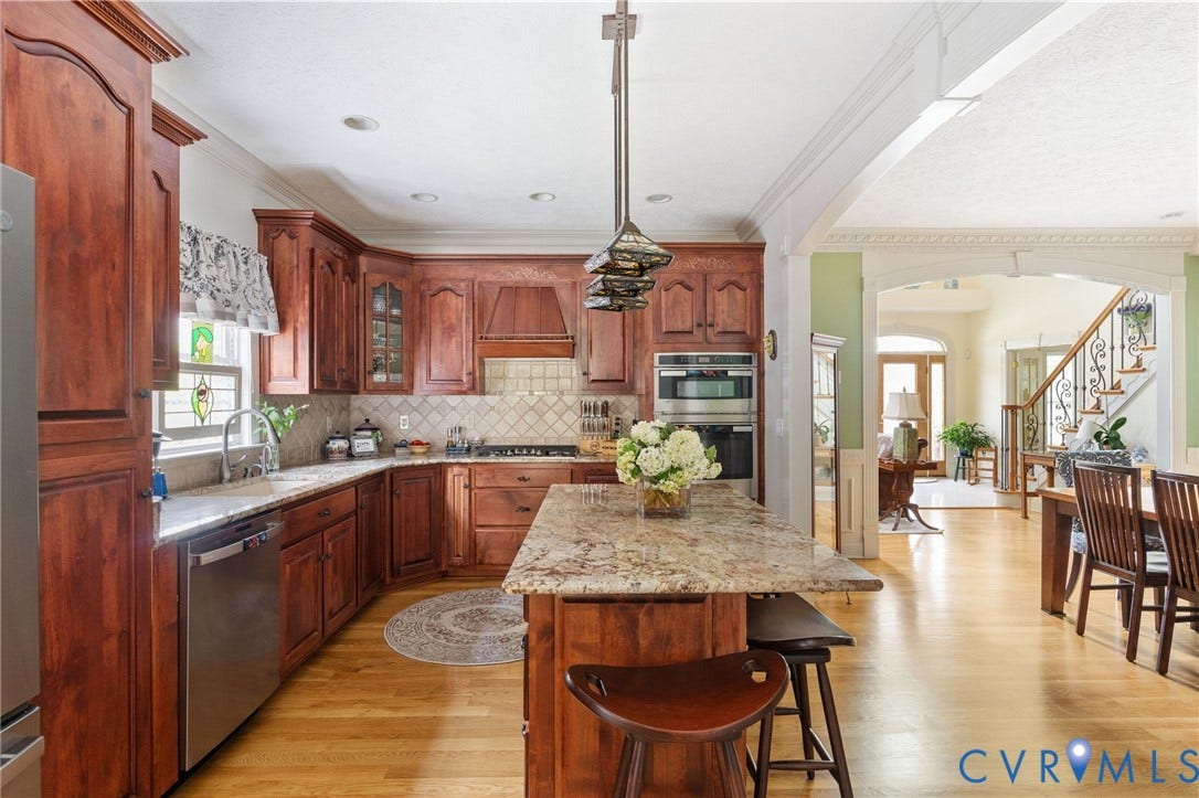 Chef's kitchen showcasing rich wood cabinetry, granite countertops, stainless steel appliances, and a spacious island with seating