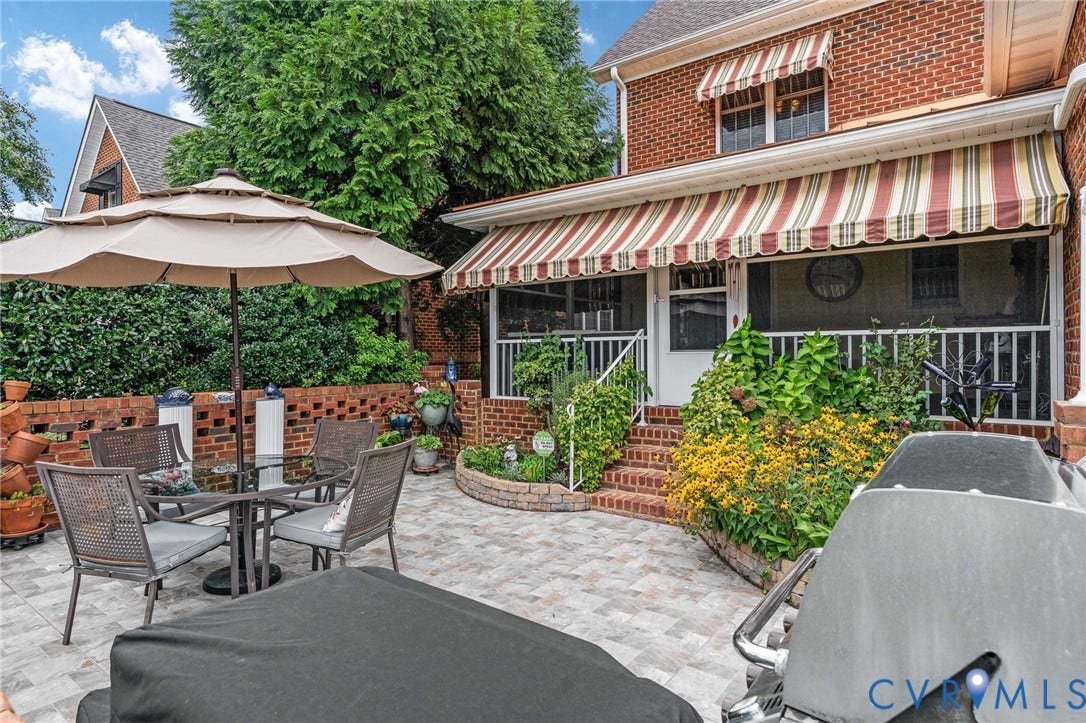 Brick exterior property featuring a screened porch with striped awnings, and an adjacent paver patio with a brick retaining wall and mature plantings