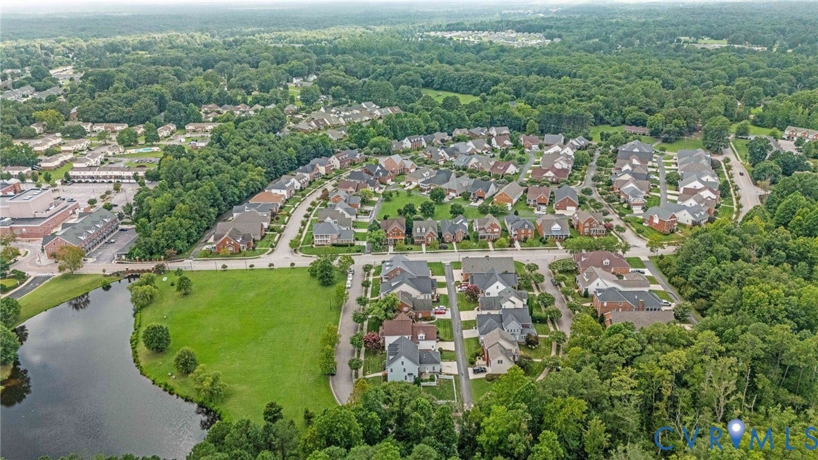 Residential community featuring a variety of single-family homes, mature tree coverage, a central pond, and commercial buildings