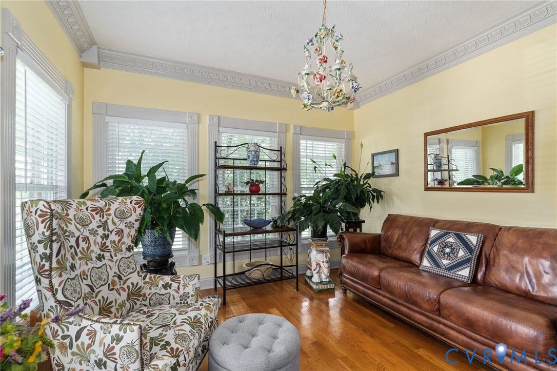 Hardwood flooring throughout featuring multiple windows with blinds, detailed ceiling molding, and an ornate chandelier