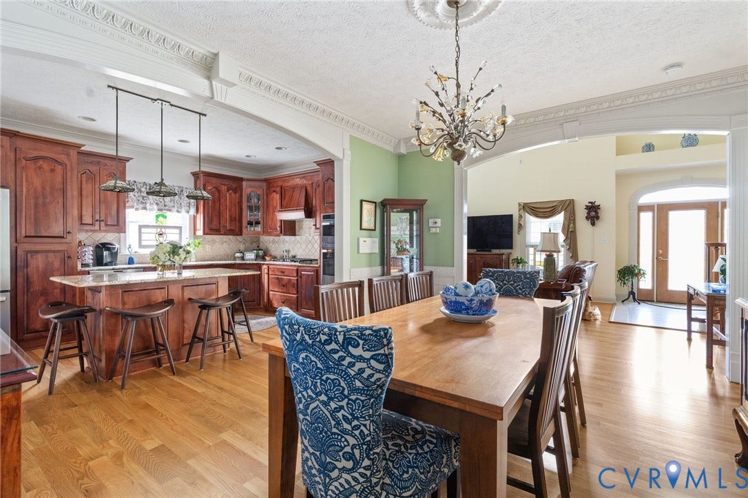 Open-concept dining and kitchen area featuring rich wood cabinetry, a substantial wood-finish dining table with upholstered seating, pendant lighting, and hardwood flooring throughout