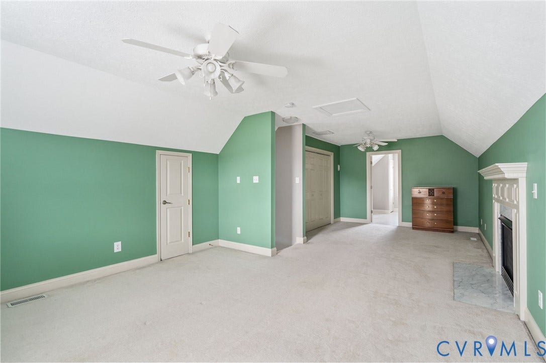 Spacious room featuring vaulted ceilings, a built-in fireplace with a stone hearth, soft carpet flooring, and two ceiling fans
