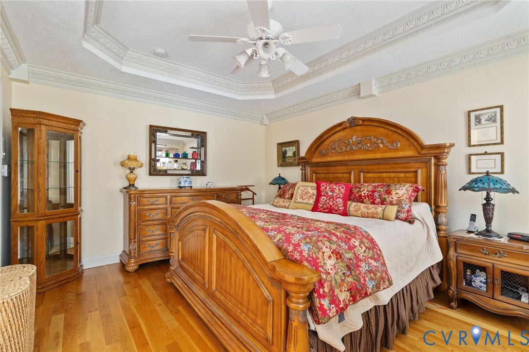 Recessed ceiling with decorative molding, ceiling fan, and wood-finish flooring
