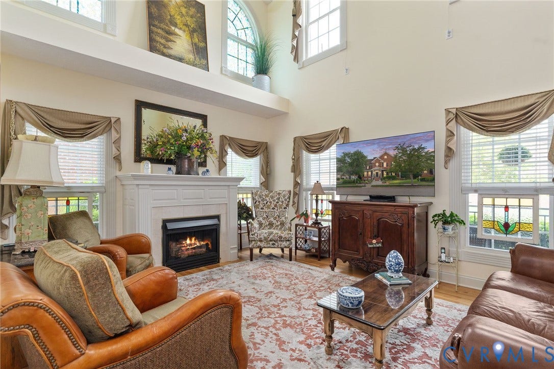 Vaulted living space featuring a white mantel fireplace, hardwood flooring, and multiple windows including upper arch-top windows