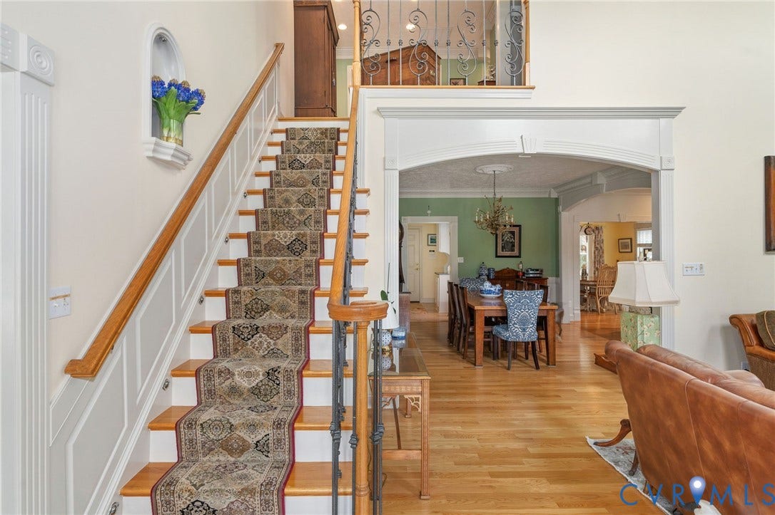 Hardwood flooring spans an open-concept interior featuring a grand staircase with a decorative runner and wrought iron balusters