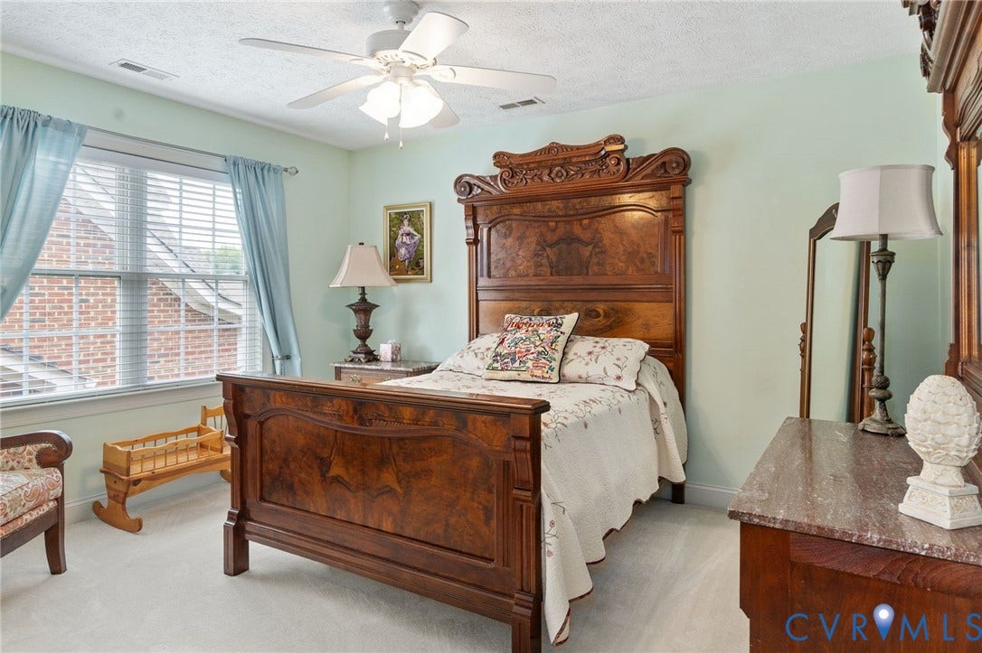 Light-filled room featuring a broad window with blinds, ceiling fan, and light-colored carpeting