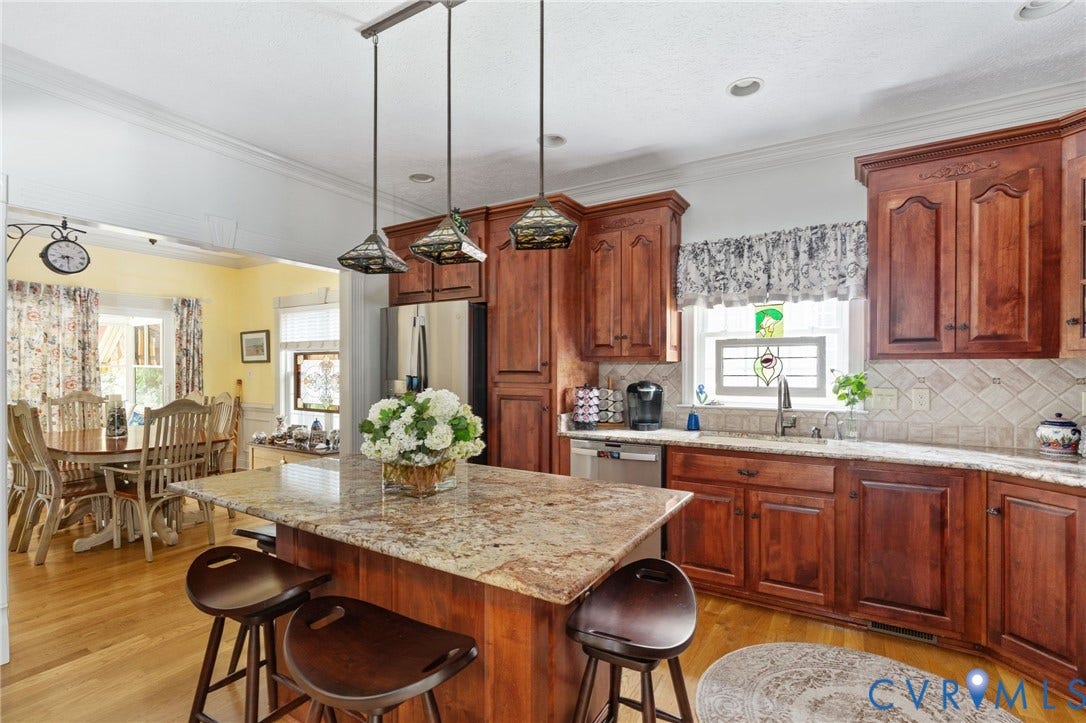 Kitchen featuring a breakfast bar island with granite countertop, wood-finish flooring, cherry wood cabinetry, stainless steel appliances, and tile backsplash