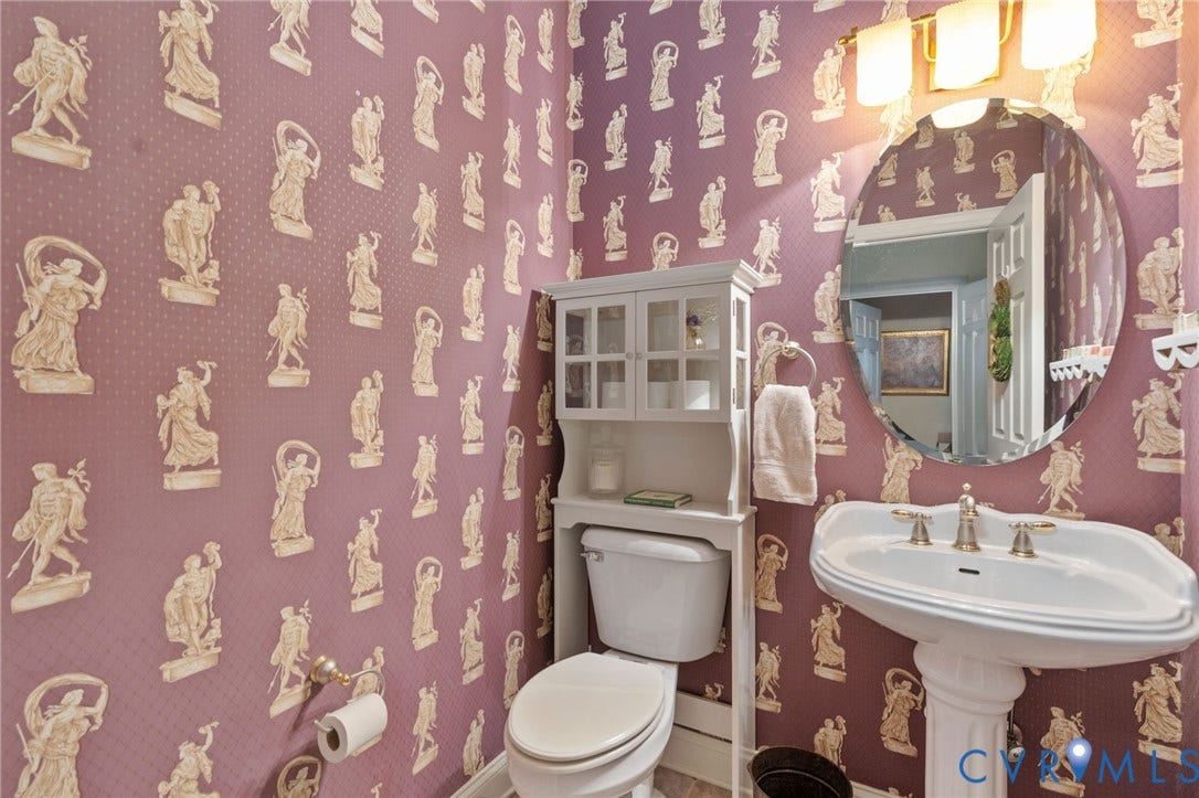 Pedestal sink with brass-toned fixtures, a circular mirror, and a wall-mounted light fixture with three sconces