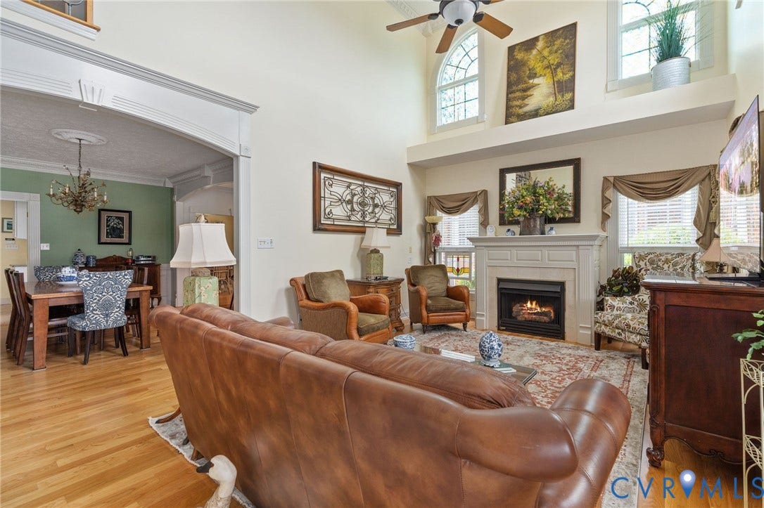 Spacious living room featuring high vaulted ceilings, a ceiling fan, a prominent fireplace with a decorative mantel, and wood-finish flooring