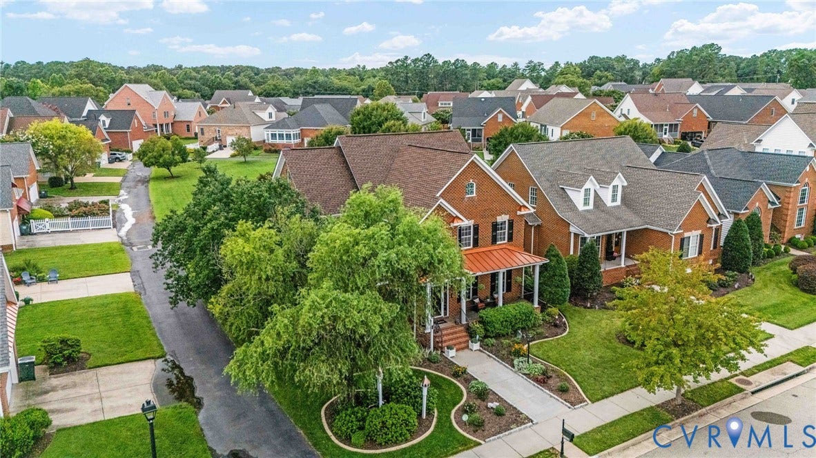 Brick Colonial residence showcasing a manicured front landscape with mature shade trees, circular driveway, and professionally maintained lawn