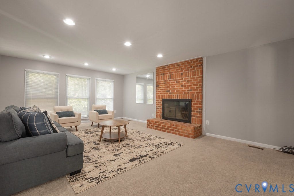 Brick fireplace with a black firebox, recessed lighting, neutral carpeting, and multiple windows with roller shades