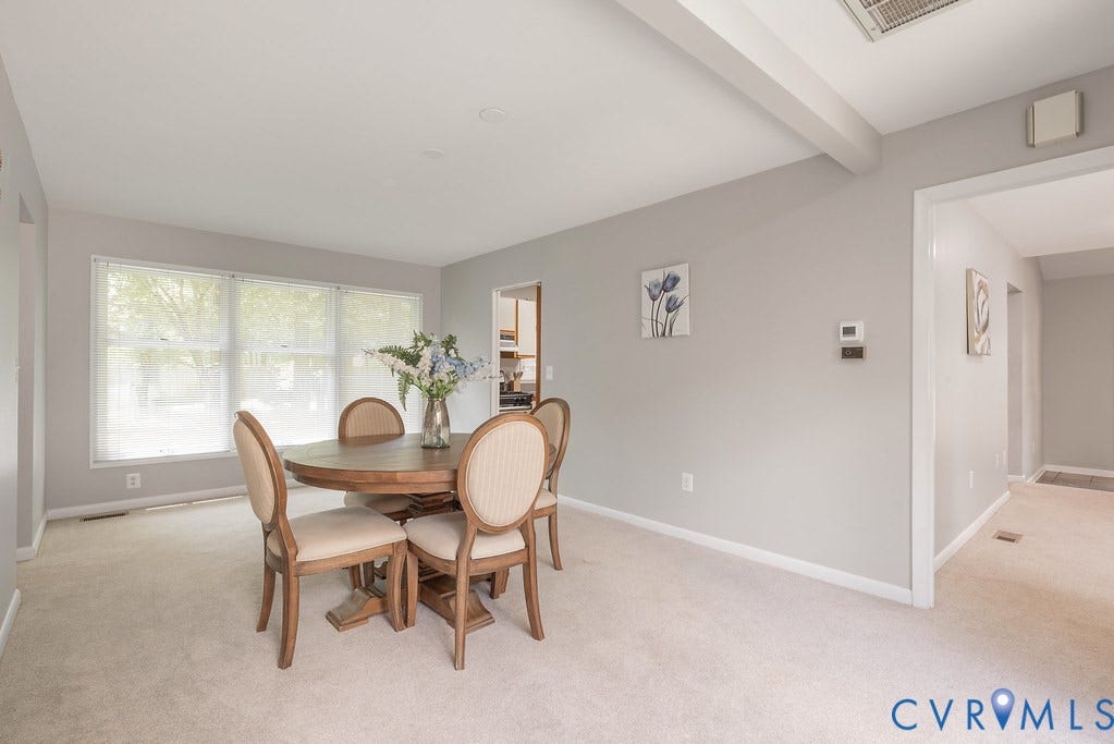 Dining area with light-toned carpeting, neutral wall color, triple window installation, and a ceiling beam accent