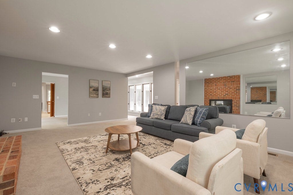 Recessed lighting illuminates the living area, featuring a brick fireplace and a large wall-mounted mirror