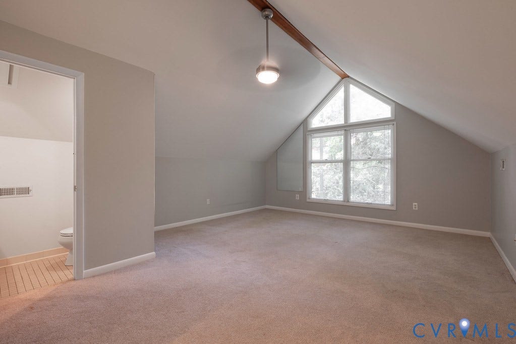 Vaulted ceiling with exposed wood beam, architectural transom window, carpeted flooring, and a neutral color palette