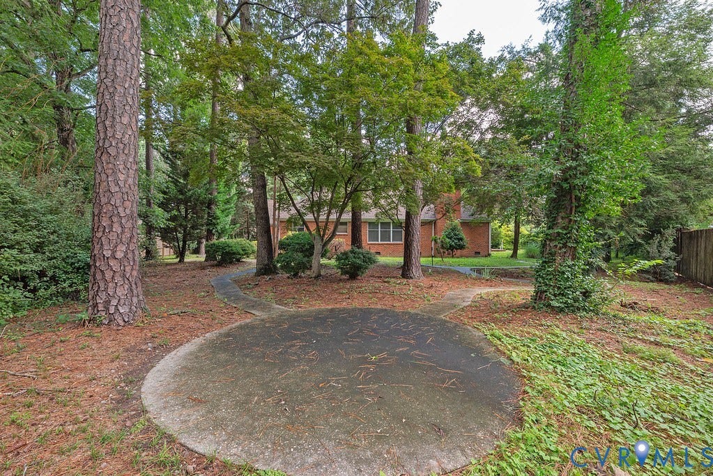 Expansive outdoor space featuring mature trees, a wooden privacy fence, and a concrete patio