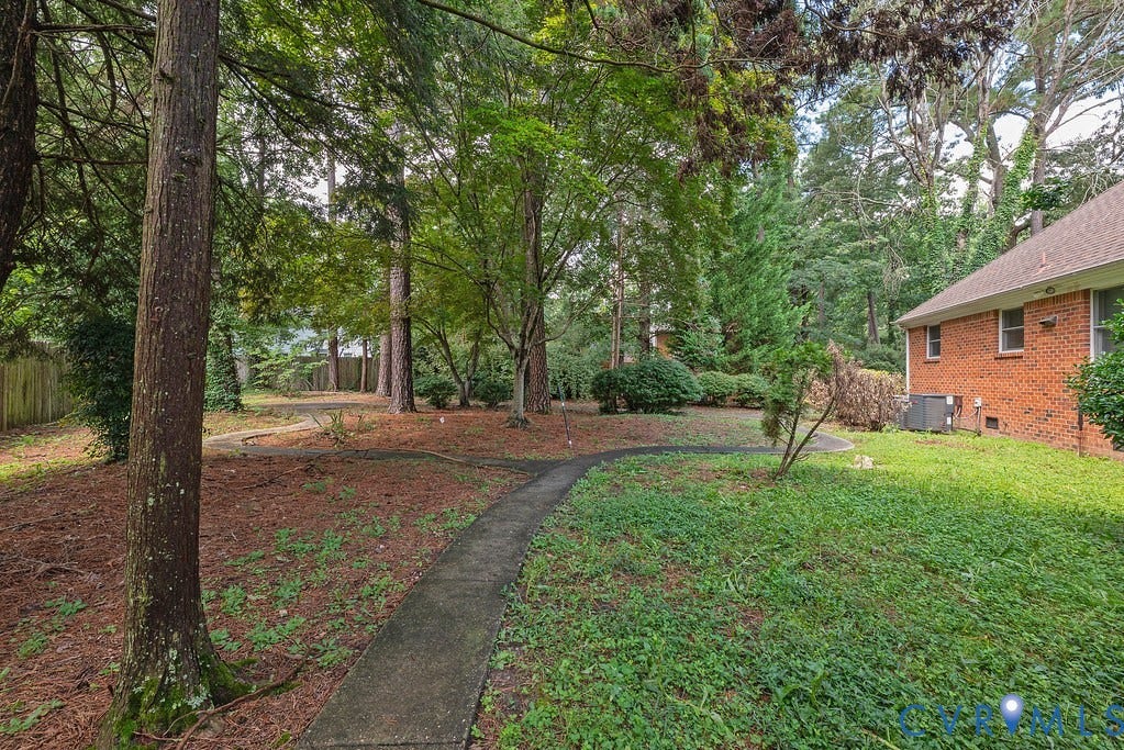 Mature trees, concrete pathway, brick exterior, natural ground cover, partial privacy fencing