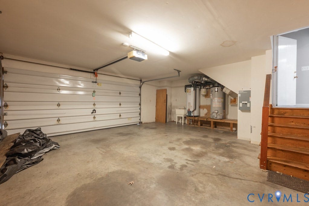 Attached garage featuring a white sectional door, concrete flooring, and an exposed wood staircase