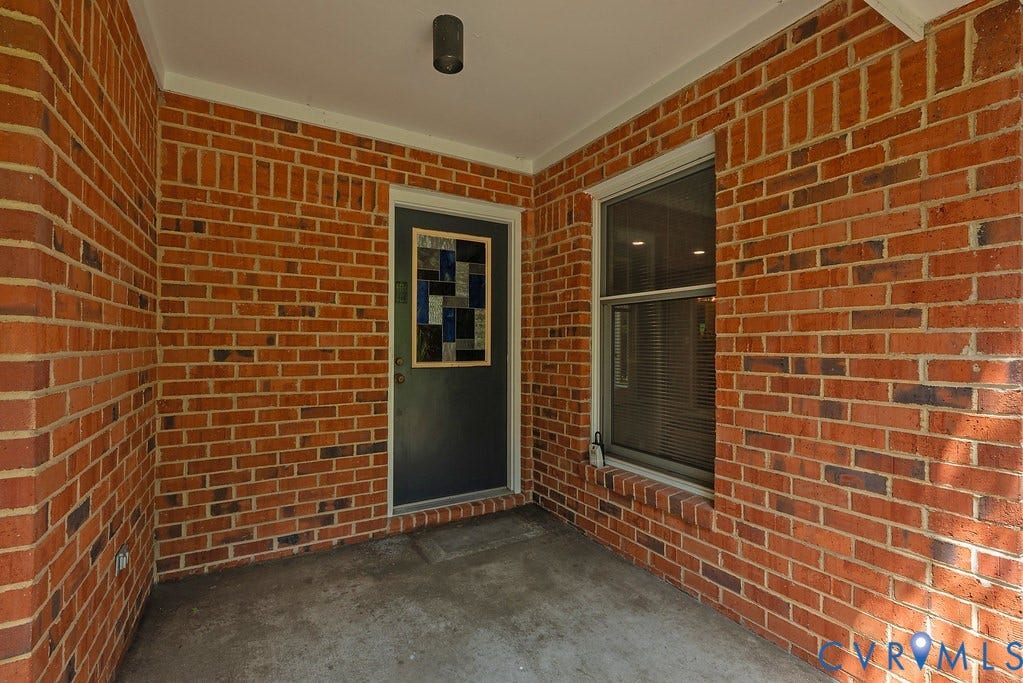 Brick exterior with concrete flooring, accented by a dark-paneled door with decorative glass