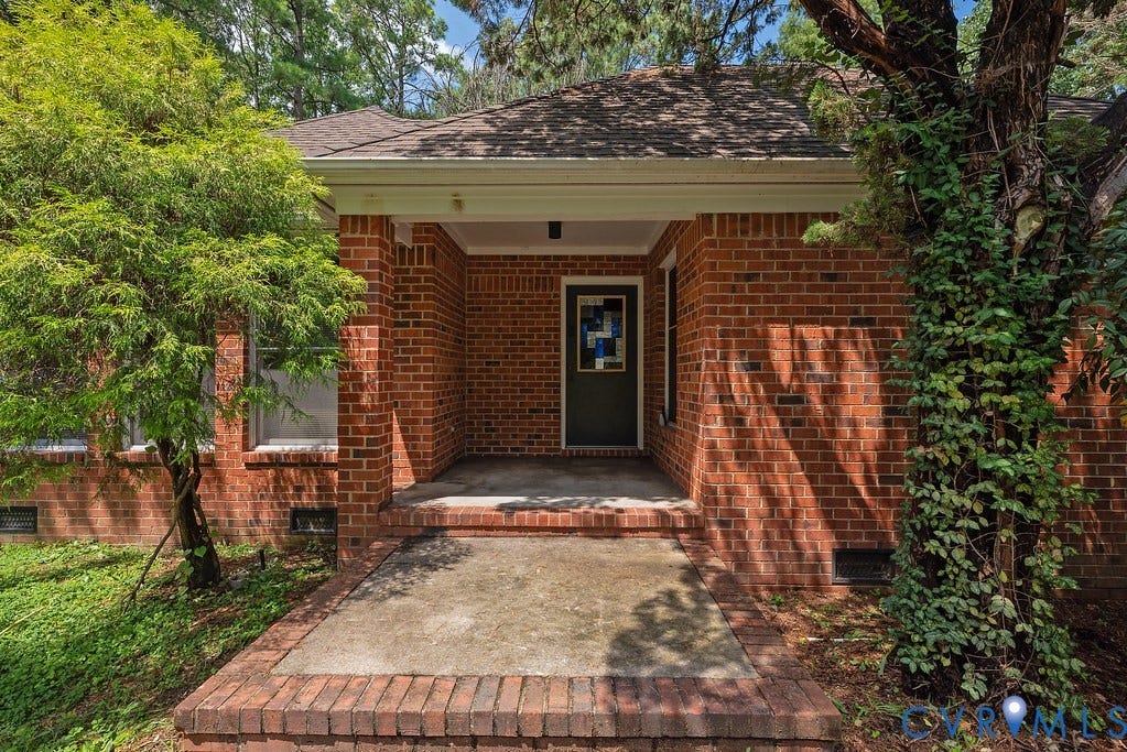 Brick exterior with a covered porch, dark entry door, and perimeter landscaping